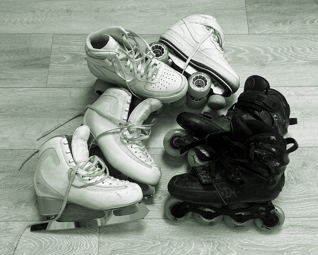 A pair of figure skates, quad skates, and freestyle inline skates together on the floor.