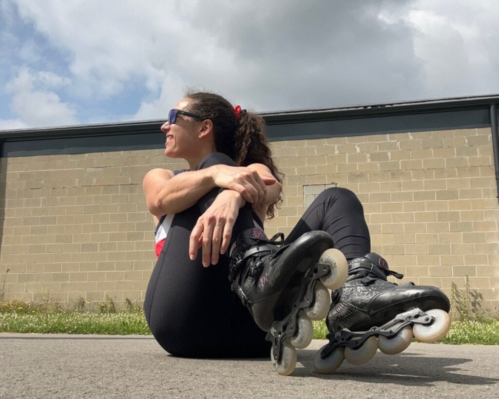 Woman wearing inline skates sitting on the asphalt, looking away from the camera and smiling.
